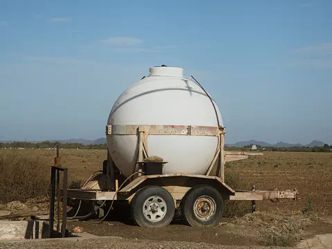A round water tank on a trailer in a dry field