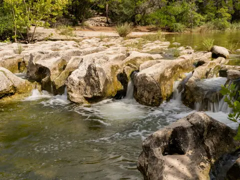 Clear water running over pale limestone ledges along a tree-lined Texas creek
