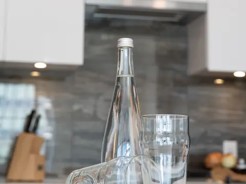 A glass bottle of water and two glasses on a bright kitchen counter