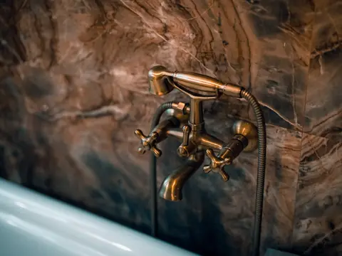 Bronze bath taps and a hand shower on a stone wall