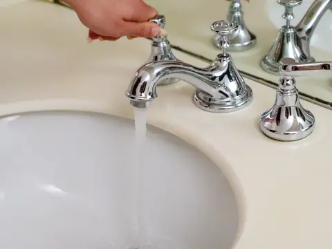A hand turning on a chrome bathroom faucet