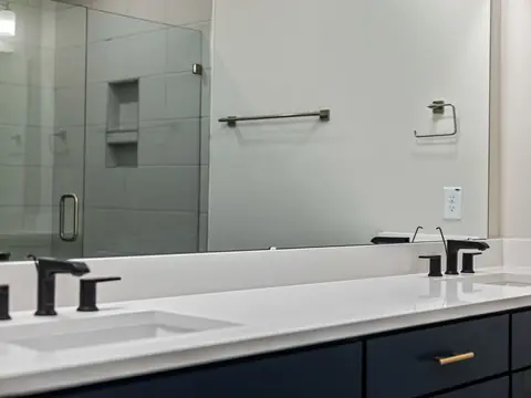 A bathroom vanity with black faucets and a wide mirror