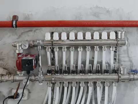 A manifold of steel pipes and valves with pressure gauges on a wall